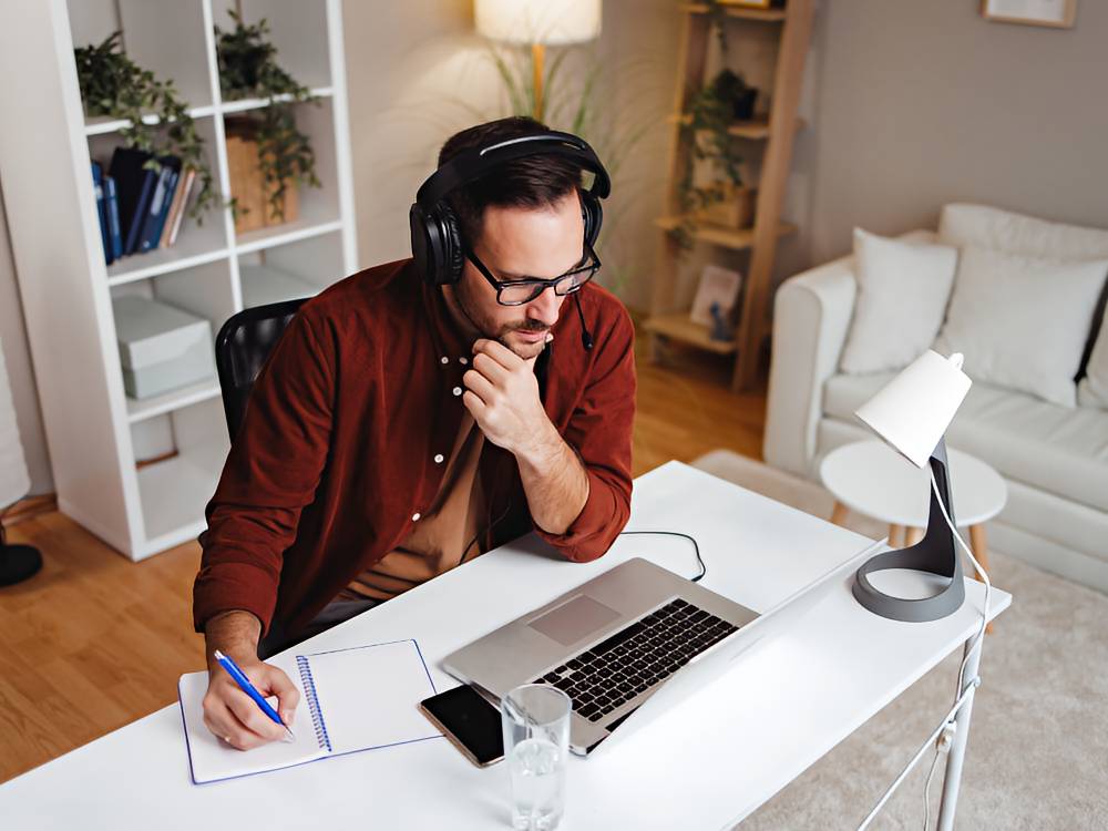 Man sitting at his desk, taking notes in front of a laptop.